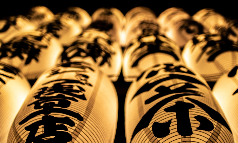 Rangées de lanternes de papier chōchin allumées, peintes de kanji noirs, dans une rue japonaise