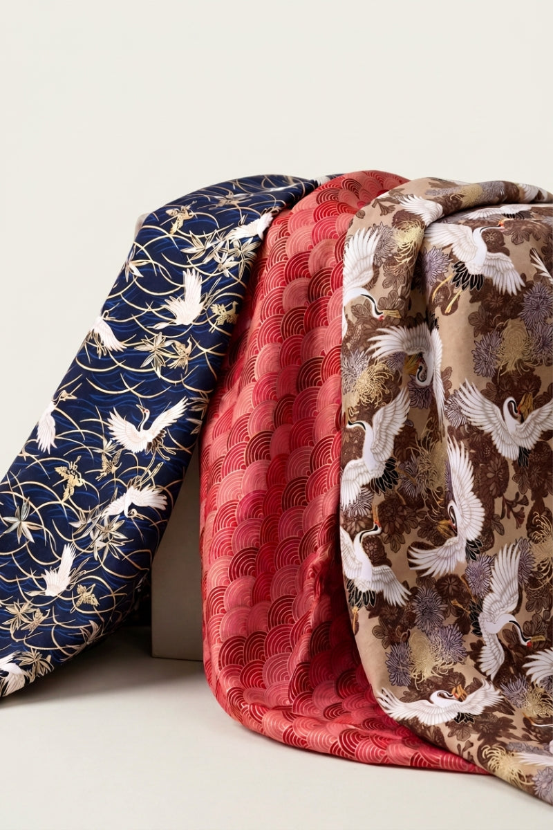 Collection furoshiki : trois carrés de tissu japonais drapés côte à côte, grues en vol sur bleu nuit, vagues seigaiha rouges et chrysanthèmes