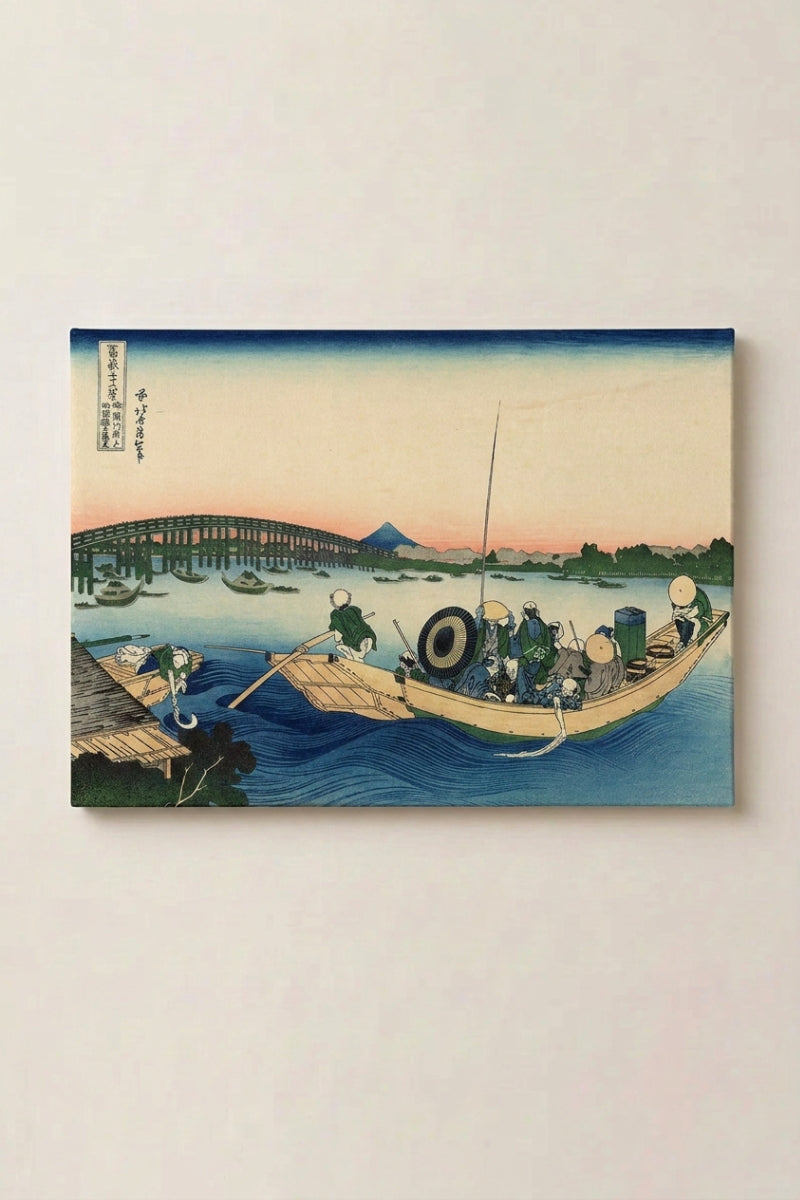 Estampe japonaise 'Ikebi' présentée en panneau encadré sur un mur beige — barque chargée glissant sous un pont au couchant rose, silhouette du mont Fuji au loin
