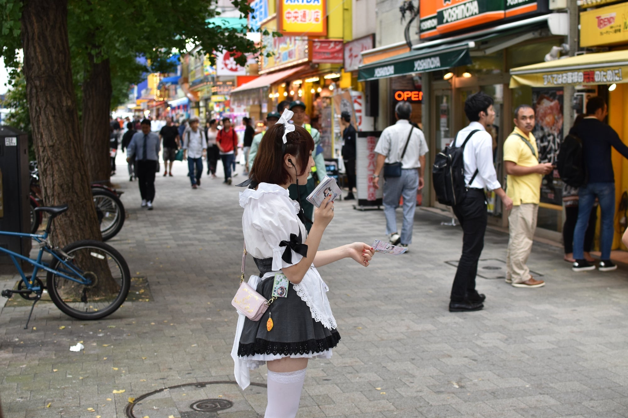 Serveuse en tenue de maid café distribuant des flyers à Akihabara, au cœur de la culture otaku et des cafés thématiques japonais.