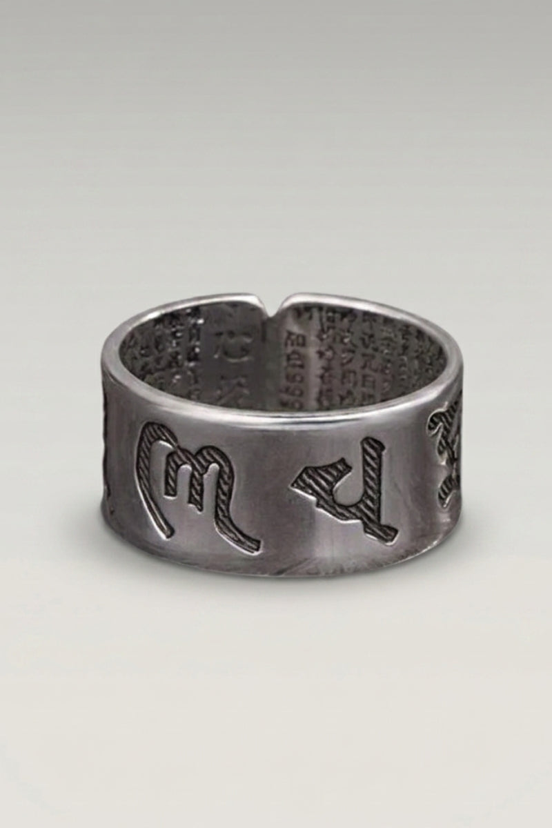 Bague 'Fujiwa' — anneau large à finition brute et sombre, caractères de mantra en relief, photo produit sur fond gris clair