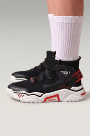 Baskets montantes 'Echizen' coloris noir — deux sangles larges, col rembourré, détails rouges, portées avec chaussettes blanches sur fond studio gris