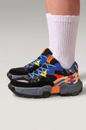 Baskets chunky 'Tsuruga' coloris noir — panneaux contrastés bleu et orange, semelle gomme, portées avec chaussettes blanches sur fond studio gris