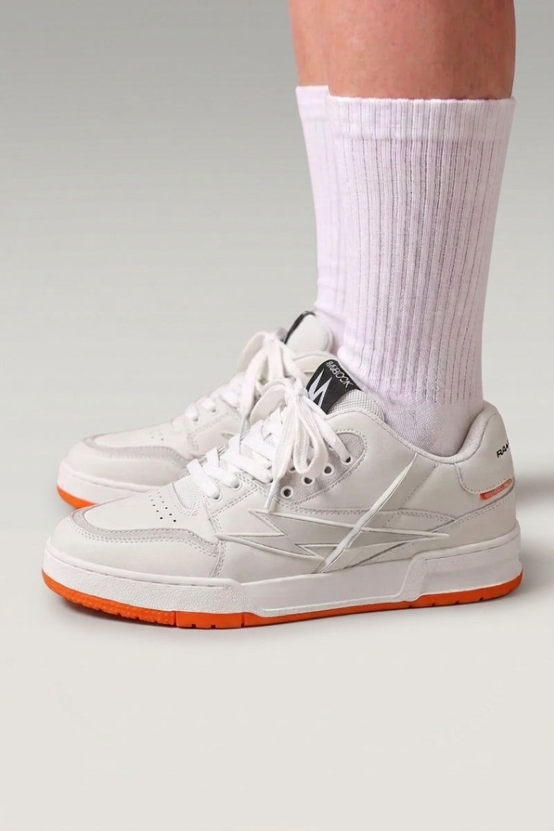 Baskets chunky 'Inazuma' coloris orange — tige blanc et gris posée sur une semelle monochrome vive, portées avec chaussettes blanches sur fond studio gris