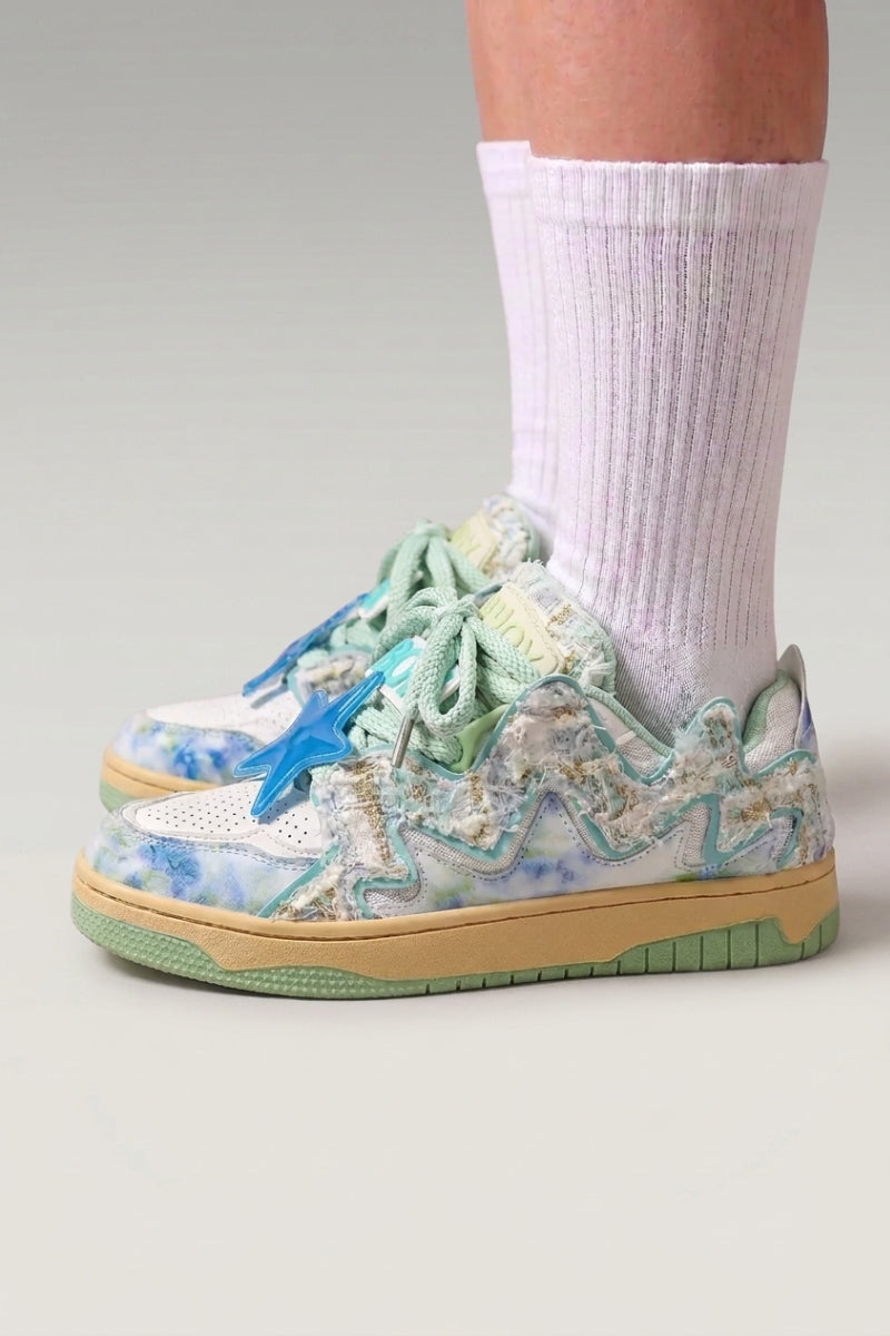 Baskets basses 'Kasumi' coloris vert — graffiti peint sur toute la tige, semelle teintée assortie, portées avec chaussettes blanches sur fond studio gris