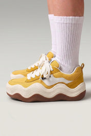 Baskets à plateforme 'Nami' coloris jaune — semelle plateforme découpée en vague ondulée bicolore, portées avec chaussettes blanches sur fond studio gris