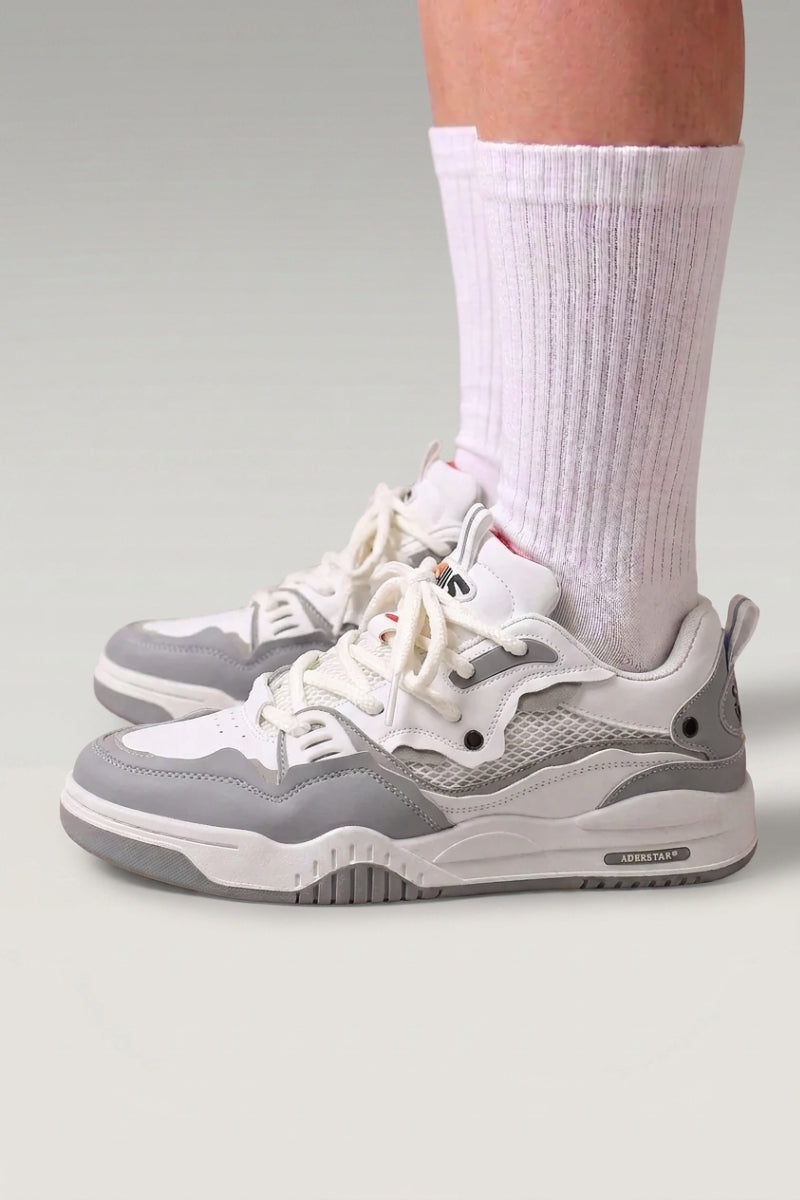 Baskets basses 'Raijin' coloris gris — panneaux de mesh superposés, semelle basse nervurée, portées avec chaussettes blanches sur fond studio gris