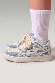 Baskets basses 'Seiryu' coloris bleu — toile délavée à motif floral fondu, semelle cupsole crème, portées avec chaussettes blanches sur fond studio gris