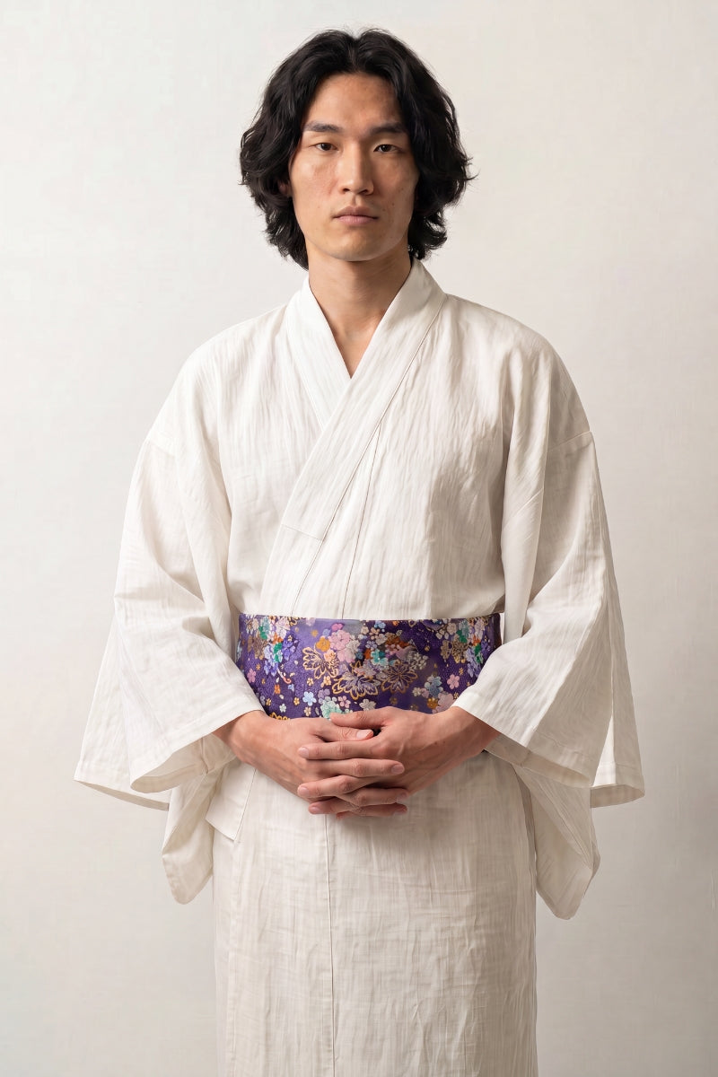 Ceinture obi 'Nadeshiko' portée à la taille sur un kimono blanc par un mannequin homme — fond violet profond couvert de fleurs polychromes rehaussées d'or