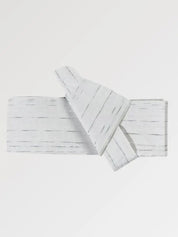 Ceinture obi 'Sakemi' pliée à plat sur fond gris, extrémités repliées l'une sur l'autre — gris très clair strié de traits blancs irréguliers