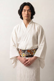 Ceinture obi 'Koshiko' portée à la taille sur un kimono blanc par un mannequin homme — brocart sombre à chrysanthèmes orange et dorés sur fond de feuillage