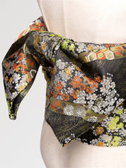 Gros plan du nœud de la ceinture obi 'Koshiko' sur un buste de mannequin — brocart sombre à chrysanthèmes orange et dorés sur fond de feuillage