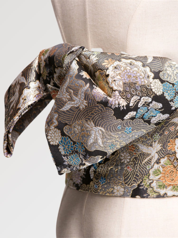 Gros plan du nœud de la ceinture obi 'Tachibana' sur un buste de mannequin — brocart noir couvert de fleurs argentées et dorées en camaïeu