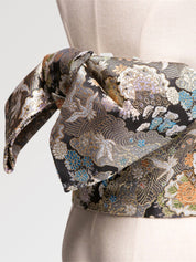 Gros plan du nœud de la ceinture obi 'Tachibana' sur un buste de mannequin — brocart noir couvert de fleurs argentées et dorées en camaïeu