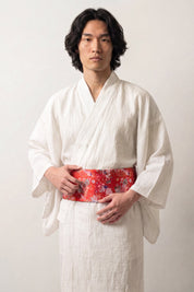 Ceinture obi 'Shochikubai' portée à la taille sur un kimono blanc par un mannequin homme — fond rouge vif couvert de petites fleurs blanches et polychromes