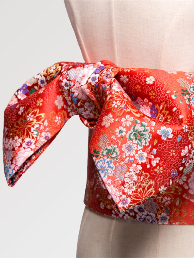Ceinture obi 'Shochikubai' nouée sur un buste de mannequin, vue de trois quarts — fond rouge vif couvert de petites fleurs blanches et polychromes