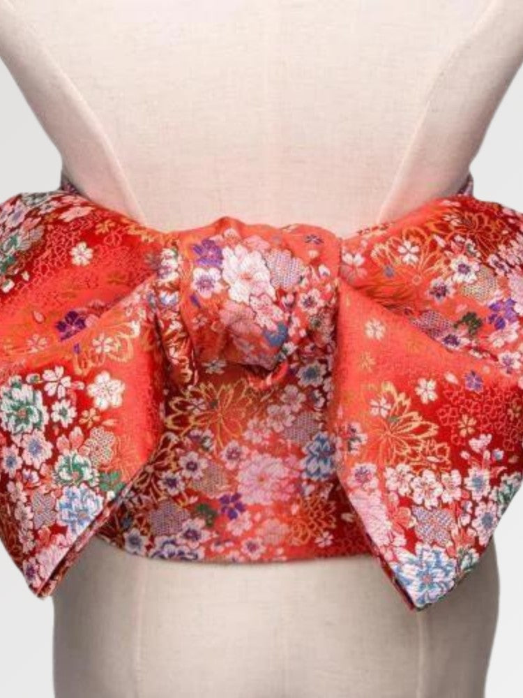 Gros plan du nœud de la ceinture obi 'Shochikubai' sur un buste de mannequin — fond rouge vif couvert de petites fleurs blanches et polychromes