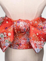 Gros plan du nœud de la ceinture obi 'Shochikubai' sur un buste de mannequin — fond rouge vif couvert de petites fleurs blanches et polychromes