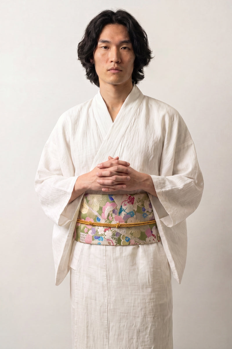 Ceinture obi 'Sakura' portée à la taille sur un kimono blanc par un mannequin homme — brocart vert pâle et doré semé de fleurs roses et de grues