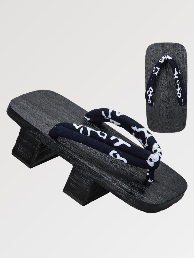 Paire de geta 'Nagano' vue de trois quarts — socle en bois noirci à deux dents, lanière bleu nuit à volutes blanches, dessous visible