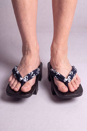 Geta japonaise 'Nagano' portée pieds nus, vue de face — lanière bleu nuit à volutes blanches sur plateforme surélevée en bois noirci