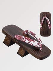 Paire de geta 'Shakori' vue de trois quarts — socle en bois foncé à deux dents, lanière rouge profond à motif cachemire blanc, dessous visible