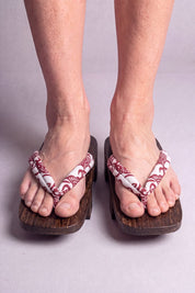 Geta japonaise 'Shakori' portée pieds nus, vue de face — lanière rouge profond à motif cachemire blanc sur plateforme surélevée en bois foncé