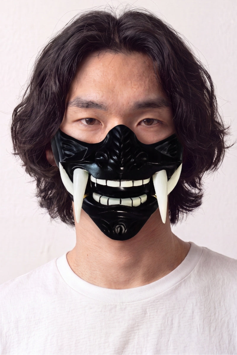 Demi-masque mempō noir porté par un mannequin sur fond clair — protection de bas de visage noire laquée, dents blanches et longues canines
