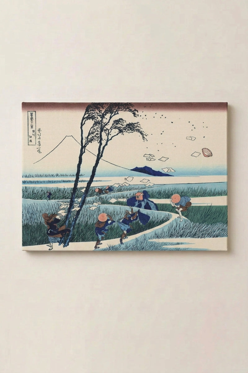 Estampe japonaise 'Kazega' en panneau encadré sur mur beige — voyageurs surpris par une rafale dans un champ, feuilles de papier envolées, Fuji à l'horizon
