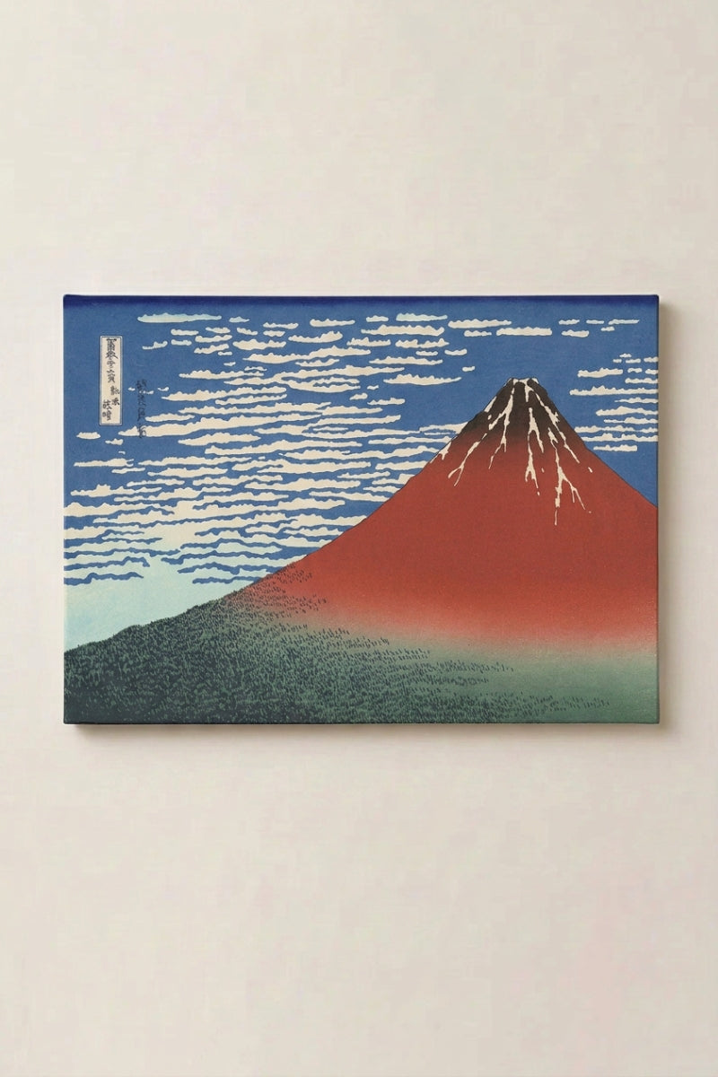 Estampe japonaise 'Okoshita' en panneau encadré sur mur beige — mont Fuji écarlate se détachant sur un ciel bleu strié de nuages blancs, forêt sombre à sa base