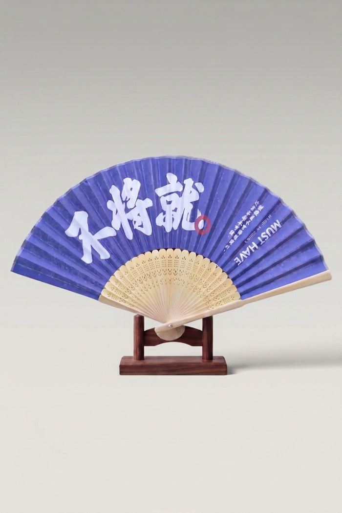 Éventail pliant japonais 'Honiko' ouvert sur son support — large calligraphie blanche au pinceau sur feuille bleu indigo, montures en bambou clair ajouré