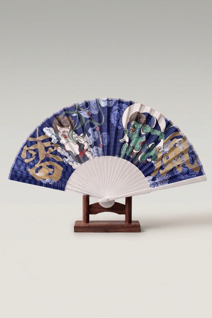 Éventail pliant japonais 'Fuurai' ouvert sur son support — Fujin et Raijin de part et d'autre de caractères dorés sur feuille indigo