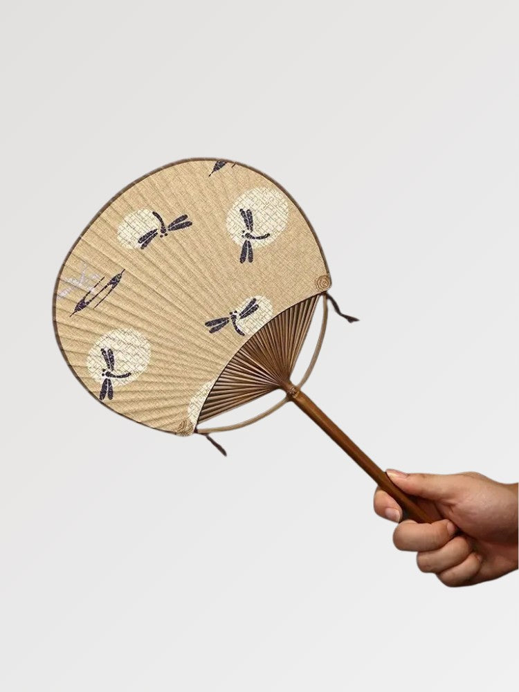 Éventail uchiwa japonais 'Shoji' modèle 10, tenu en main — fond beige à motifs d'éventails et de libellules, manche en bambou
