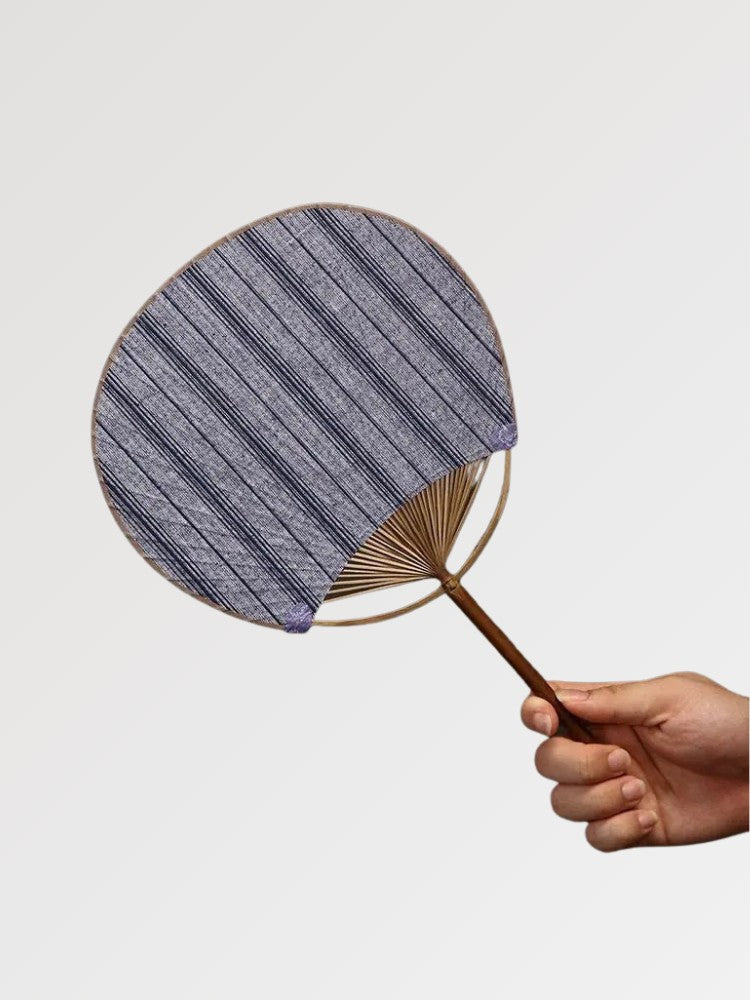 Éventail uchiwa japonais 'Shoji' modèle 2, tenu en main — toile tissée gris-bleu clair à rayures serrées, manche en bambou et cerclage rond