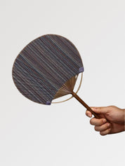 Éventail uchiwa japonais 'Shoji' modèle 6, tenu en main — toile tissée gris chiné à rayures irrégulières, manche en bambou et cerclage rond