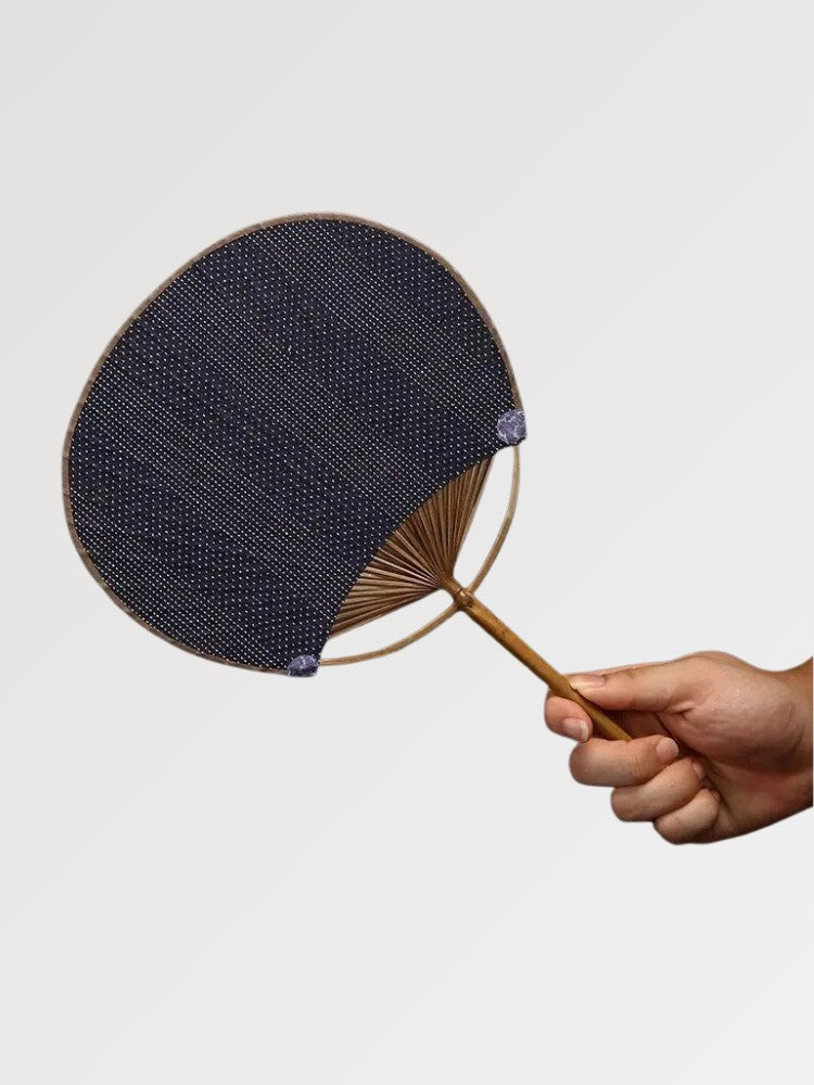 Éventail uchiwa japonais 'Shoji' modèle 7, tenu en main — toile tissée bleu ardoise à rayures fines et régulières, manche en bambou et cerclage rond