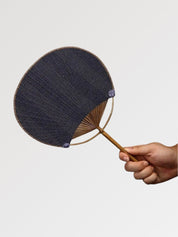 Éventail uchiwa japonais 'Shoji' modèle 7, tenu en main — toile tissée bleu ardoise à rayures fines et régulières, manche en bambou et cerclage rond