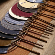 Éventails uchiwa 'Shoji' alignés à plat sur un tatami — dix coloris de toile tissée, manches en bambou tournés dans le même sens