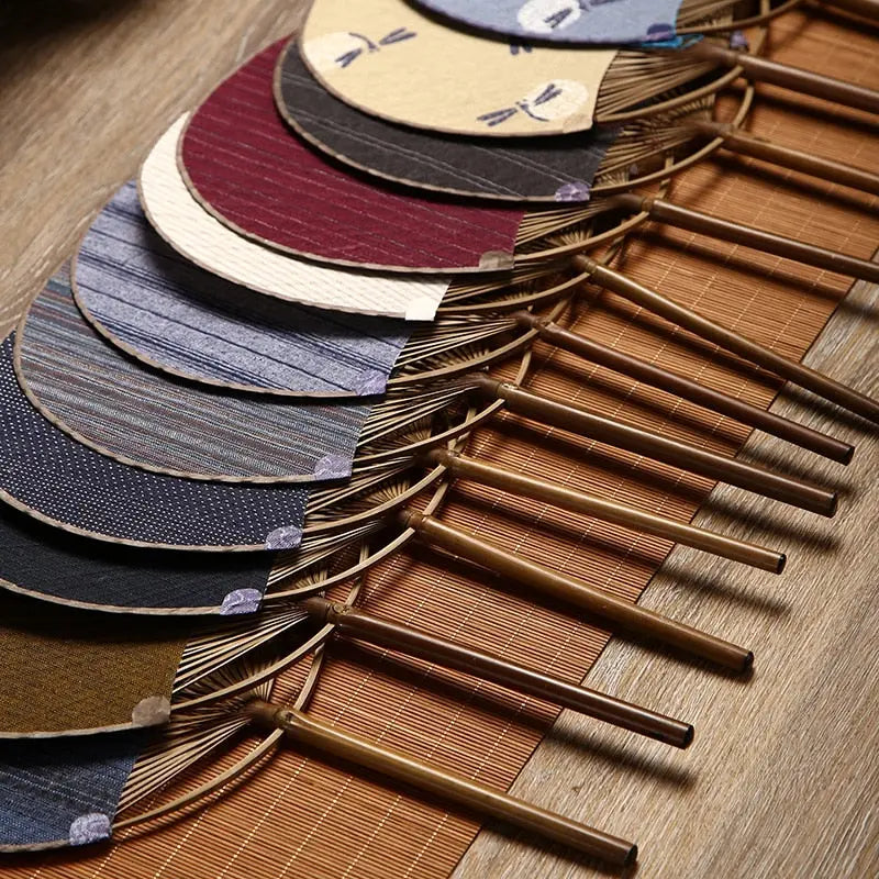 Éventails uchiwa 'Shoji' alignés à plat sur un tatami — dix coloris de toile tissée, manches en bambou tournés dans le même sens