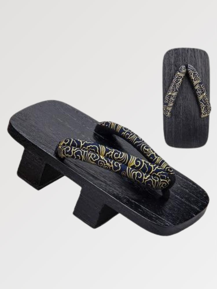 Paire de geta 'Tokoname' vue de trois quarts — socle en bois noirci à deux dents, lanière sombre à arabesques dorées, dessous visible
