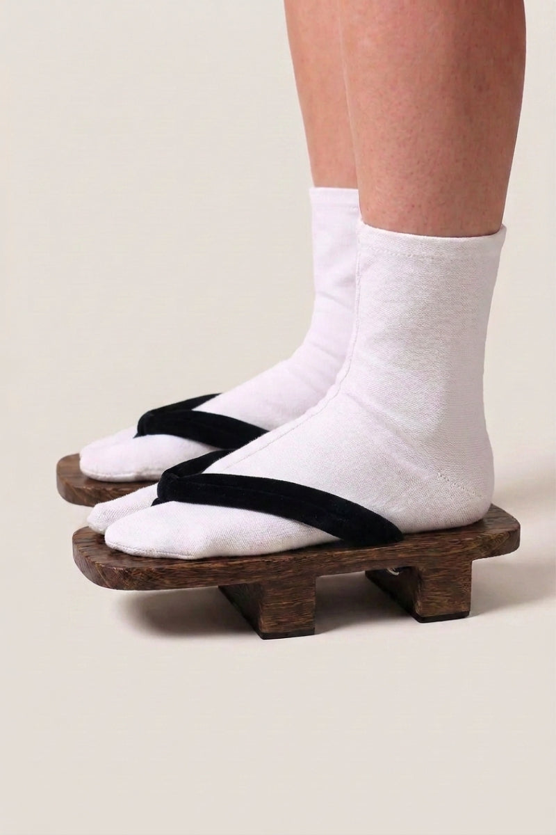 Geta japonaise 'Iwakura' portée avec des chaussettes tabi blanches, vue de profil — plateforme en bois foncé, lanière noire unie