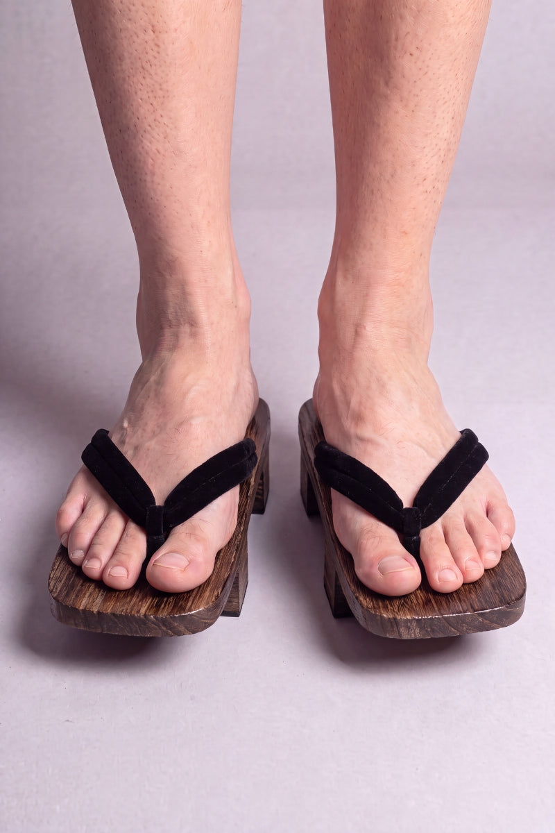 Geta japonaise 'Iwakura' portée pieds nus, vue de face — lanière noire unie sur plateforme surélevée en bois foncé