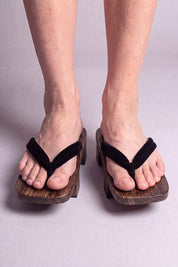 Geta japonaise 'Iwakura' portée pieds nus, vue de face — lanière noire unie sur plateforme surélevée en bois foncé
