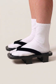 Geta japonaise 'Hekinan' portée avec des chaussettes tabi blanches, vue de profil — plateforme en bois noirci, lanière noire mate assortie au socle