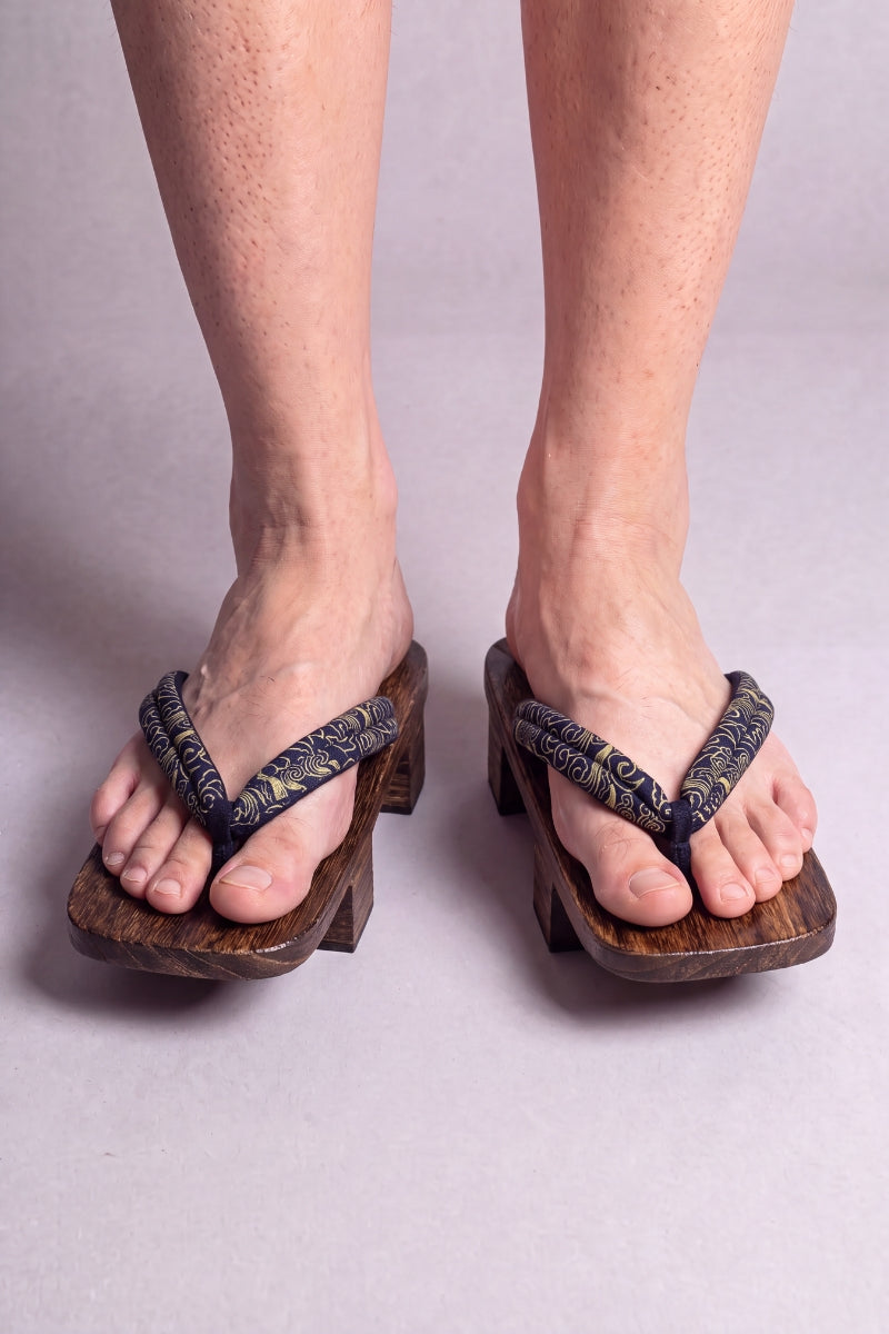Geta japonaise 'Okazaki' portée pieds nus, vue de face — lanière kaki à motif discret sur plateforme surélevée en bois foncé