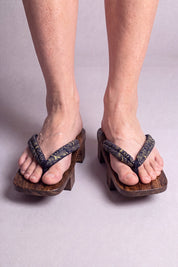 Geta japonaise 'Okazaki' portée pieds nus, vue de face — lanière kaki à motif discret sur plateforme surélevée en bois foncé