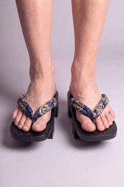 Geta japonaise 'Nagoya' portée pieds nus, vue de face — lanière bleu nuit à rinceaux dorés sur plateforme surélevée en bois noirci