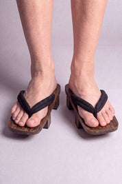 Geta japonaise 'Toyohashi' portée pieds nus, vue de face — lanière noire épaisse et rembourrée sur plateforme surélevée en bois foncé