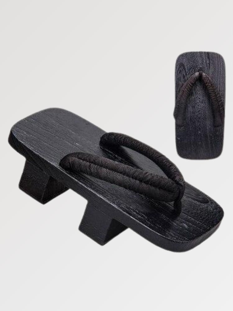 Paire de geta 'Tsushima' vue de trois quarts — socle en bois noirci à deux dents, lanière noire fine et souple, dessous visible