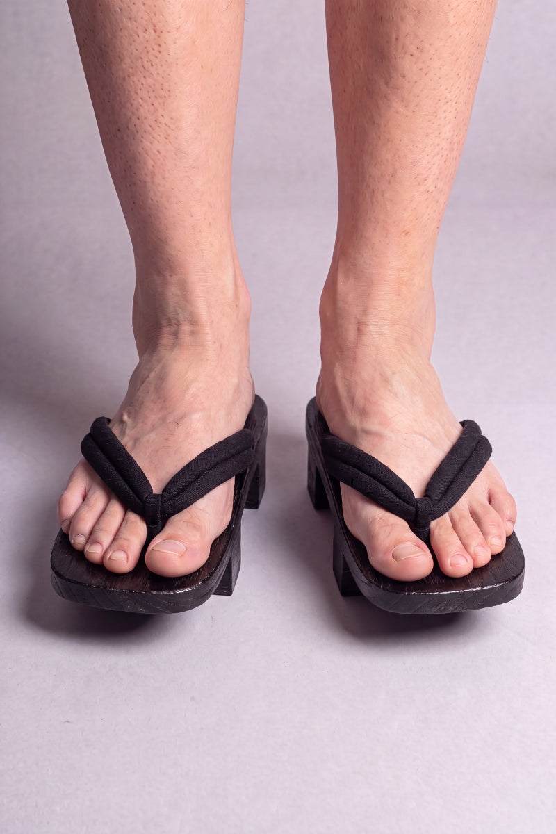 Geta japonaise 'Tsushima' portée pieds nus, vue de face — lanière noire fine et souple sur plateforme surélevée en bois noirci